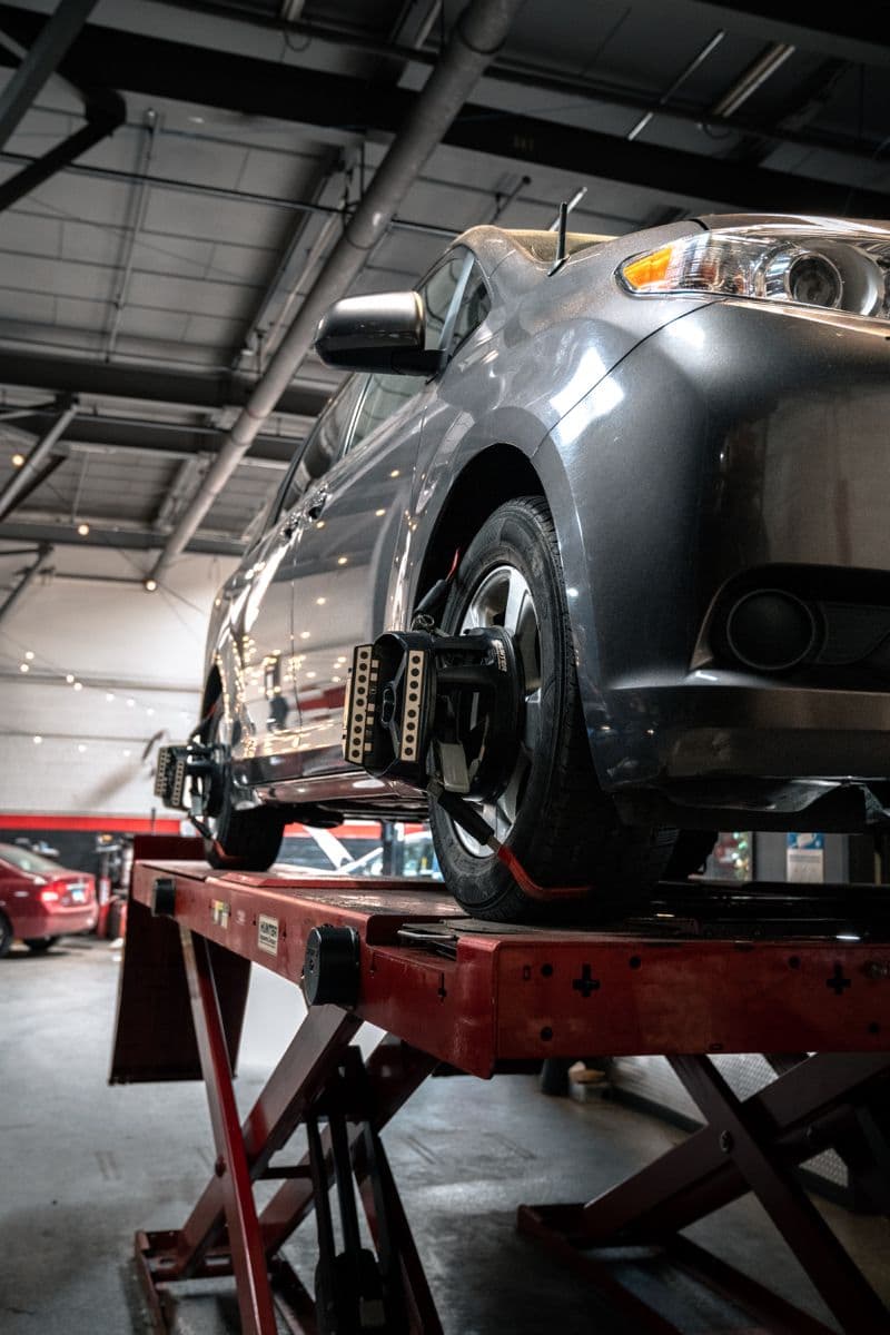 A car raised on a workshop lift with wheel-alignment heads clamped to its wheels